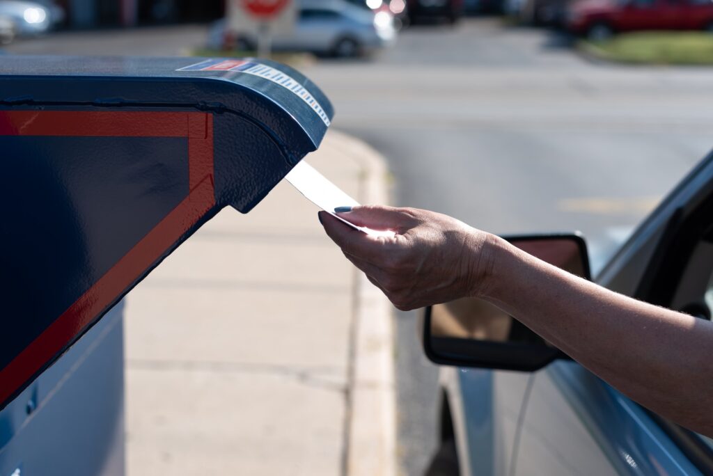 A woman is mailing an envelope in a drive thru mail box at a US Post Office - vote by mail concept