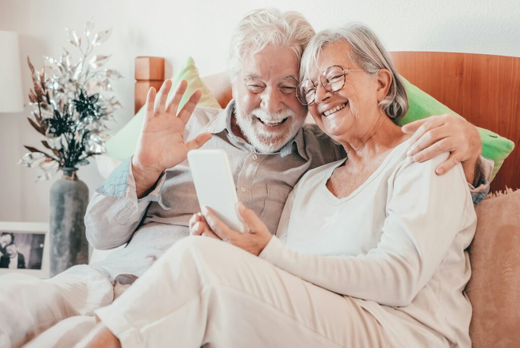 Video call concept. Happy senior couple waving hand video calling by phone while stay in bed